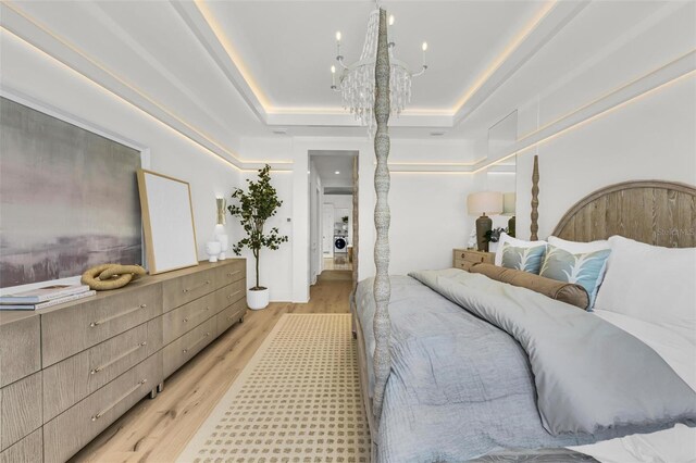 bedroom with an inviting chandelier, light hardwood / wood-style flooring, and a tray ceiling