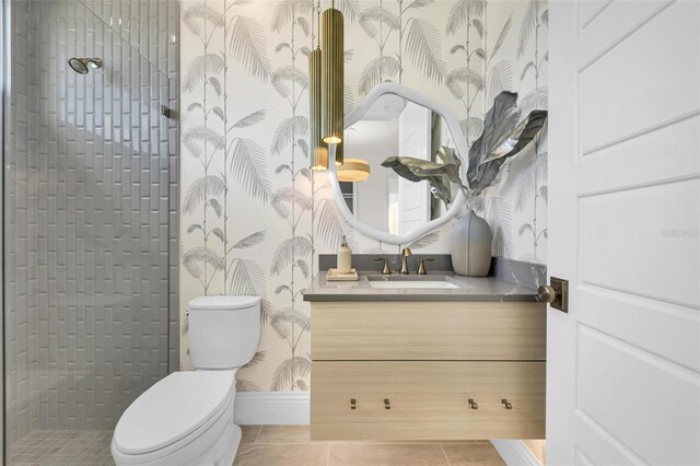 bathroom with toilet, vanity, a tile shower, and tile patterned flooring