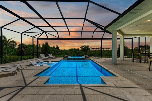 pool at dusk featuring an in ground hot tub, a patio, and a lanai