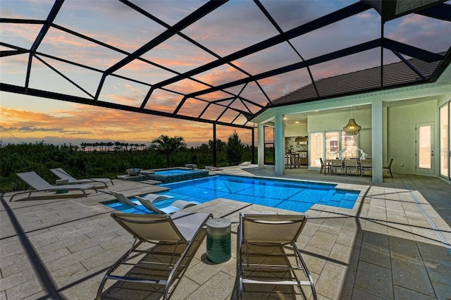 pool at dusk featuring a patio, an in ground hot tub, and glass enclosure