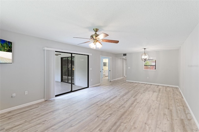 empty room featuring ceiling fan with notable chandelier, light hardwood / wood-style floors, and a textured ceiling