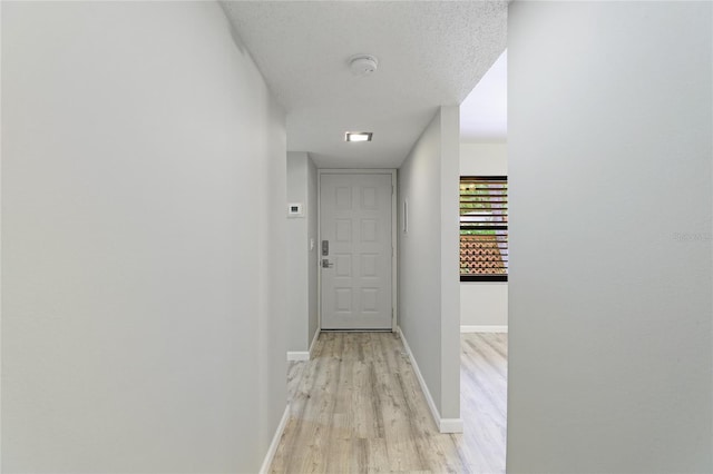 hall with a textured ceiling and light hardwood / wood-style flooring