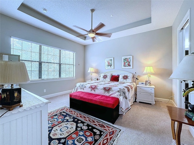 bedroom with a textured ceiling, a tray ceiling, light colored carpet, and baseboards