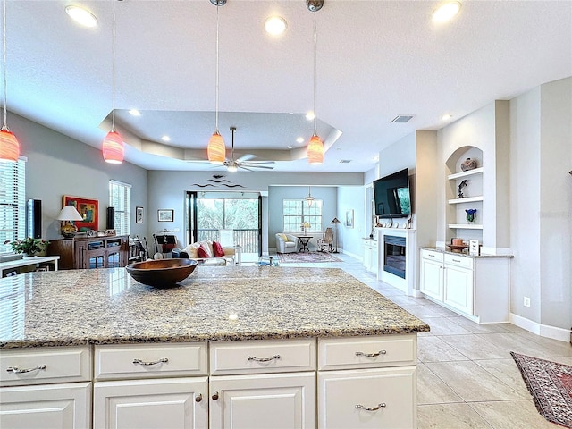 kitchen featuring baseboards, visible vents, a raised ceiling, open floor plan, and built in shelves