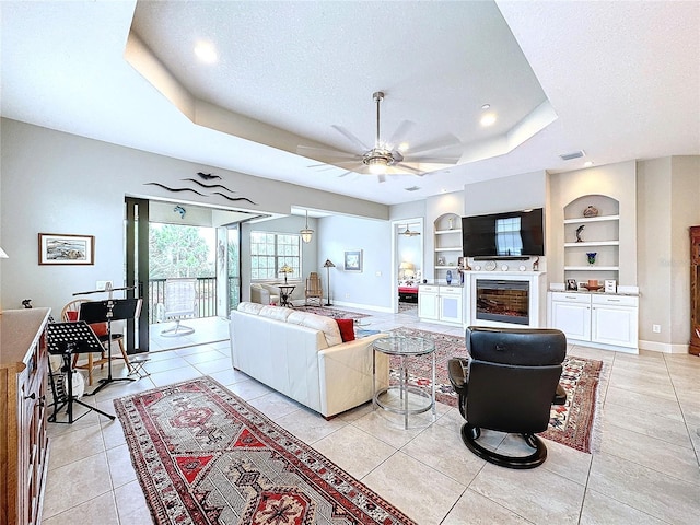 living area with light tile patterned floors, baseboards, built in features, a tray ceiling, and a textured ceiling