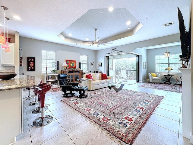 living area featuring visible vents, a raised ceiling, ceiling fan, a textured ceiling, and light tile patterned flooring