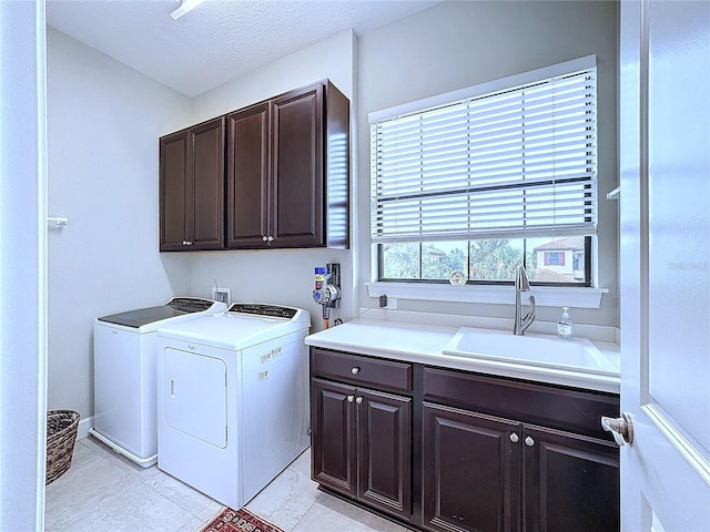 clothes washing area with cabinet space, a sink, washer and clothes dryer, and a textured ceiling