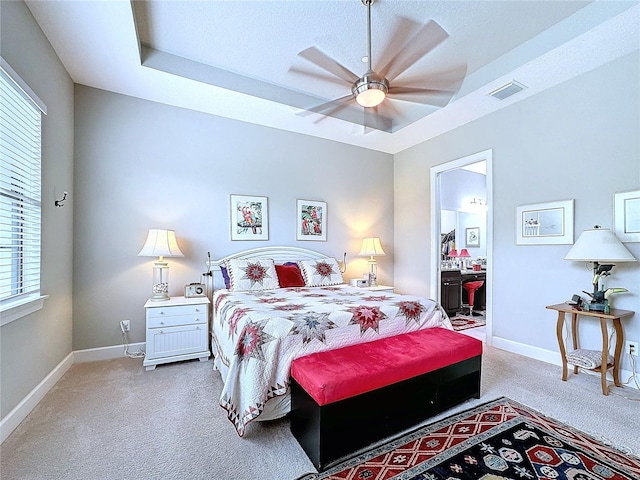 bedroom with visible vents, baseboards, connected bathroom, light colored carpet, and a tray ceiling