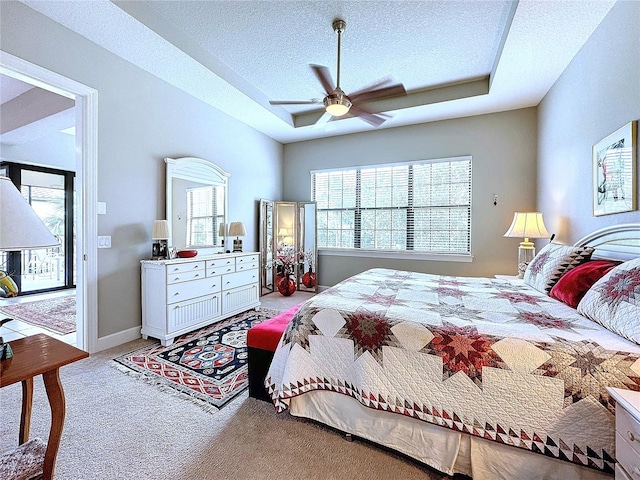 bedroom with a textured ceiling, carpet flooring, baseboards, access to exterior, and a tray ceiling