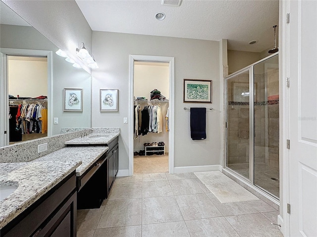 full bath with a textured ceiling, a shower stall, vanity, baseboards, and tile patterned floors