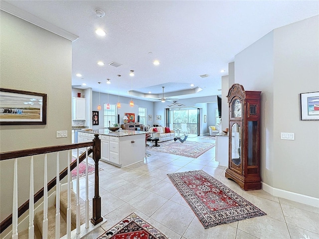 interior space with light tile patterned floors, a raised ceiling, visible vents, open floor plan, and white cabinetry