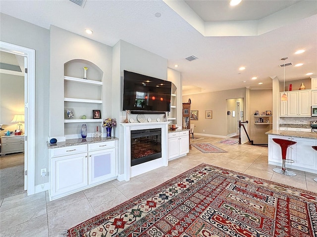 living room featuring light tile patterned floors, visible vents, built in features, baseboards, and a glass covered fireplace