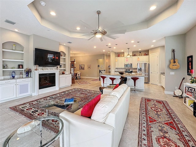 living area featuring light tile patterned floors, baseboards, built in shelves, and a tray ceiling