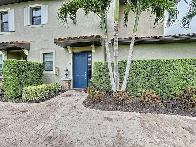 property entrance with a tiled roof, stone siding, and stucco siding