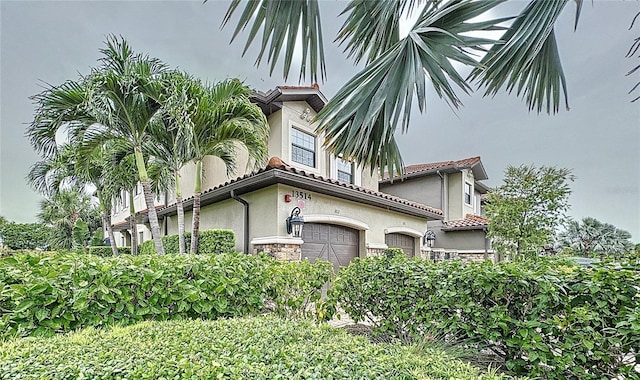 view of side of home featuring stone siding, a tile roof, and stucco siding