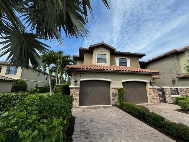 mediterranean / spanish-style house with decorative driveway, a tile roof, stucco siding, a garage, and stone siding