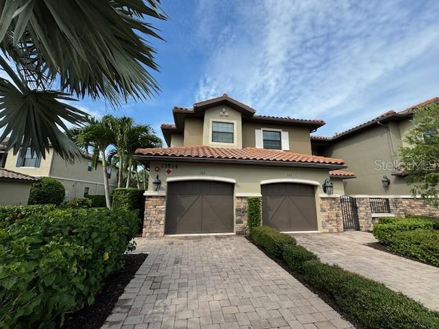 mediterranean / spanish-style house with stone siding, decorative driveway, an attached garage, and stucco siding