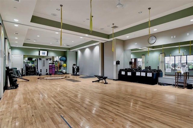 workout area featuring a raised ceiling, recessed lighting, wood finished floors, and crown molding