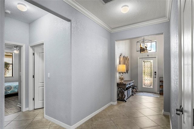 foyer featuring a textured ceiling, light tile patterned flooring, crown molding, and an inviting chandelier