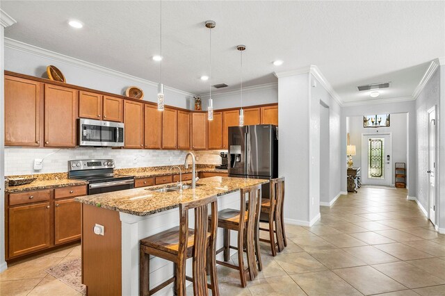 kitchen featuring a breakfast bar, stainless steel appliances, sink, hanging light fixtures, and an island with sink