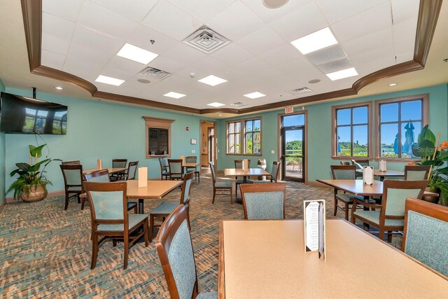 carpeted dining area with a raised ceiling and crown molding