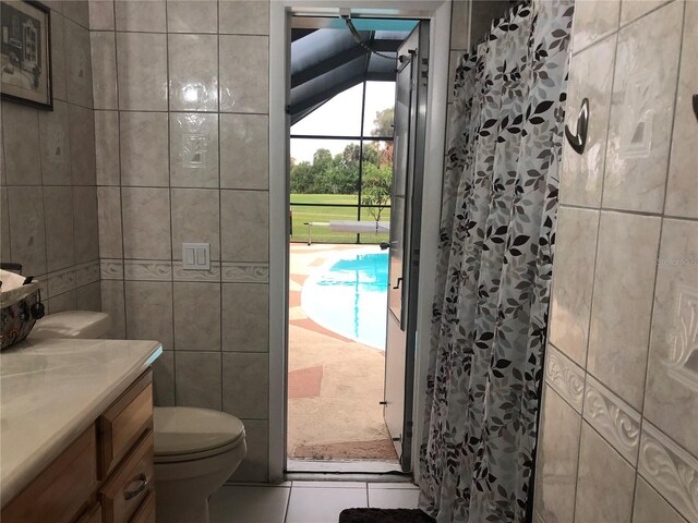 bathroom with toilet, vanity, tile patterned flooring, tile walls, and walk in shower