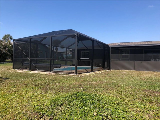 back of property featuring glass enclosure, an outdoor pool, and a lawn