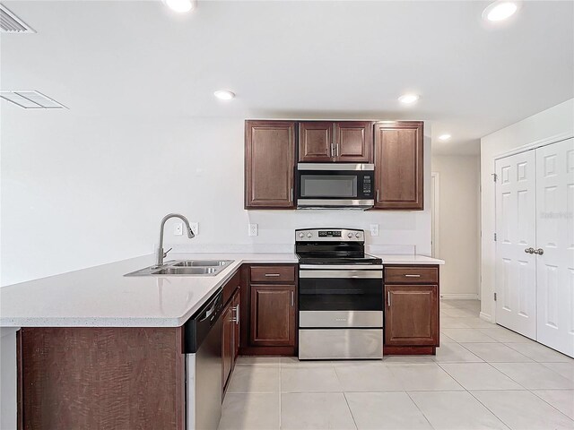 kitchen with stainless steel appliances, sink, kitchen peninsula, dark brown cabinetry, and light tile patterned flooring