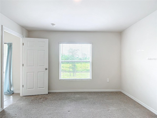 spare room featuring light carpet, baseboards, and light tile patterned floors