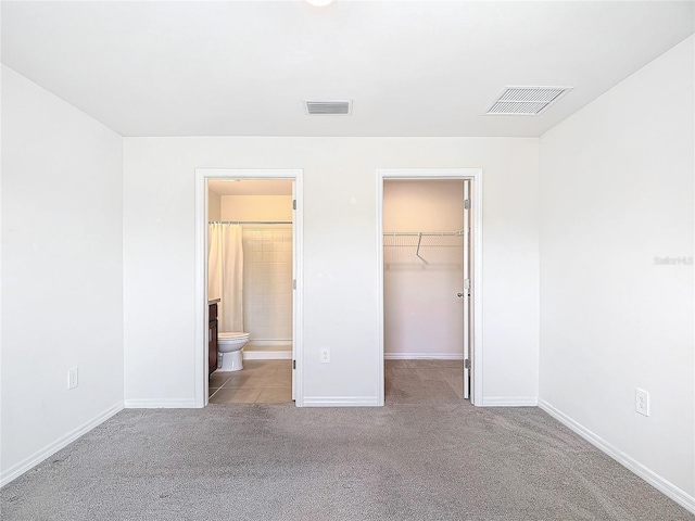 unfurnished bedroom featuring a walk in closet, visible vents, light carpet, and baseboards