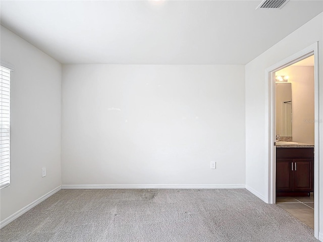 unfurnished room featuring light colored carpet, a sink, visible vents, and baseboards