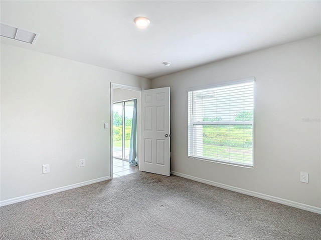 spare room featuring light colored carpet, visible vents, and baseboards