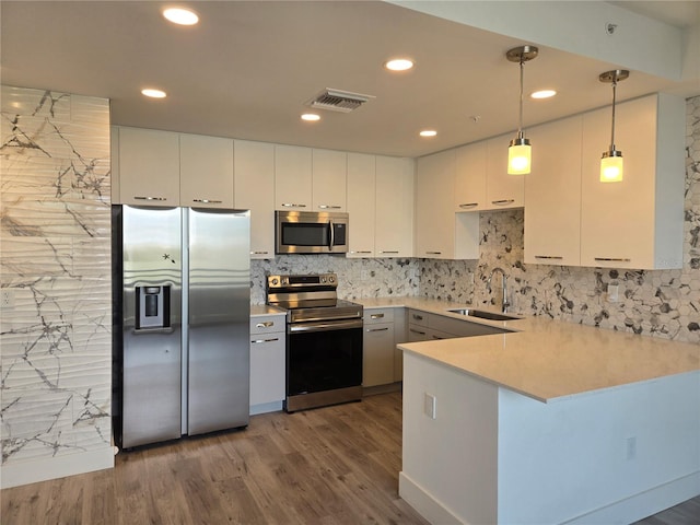 kitchen featuring kitchen peninsula, stainless steel appliances, sink, white cabinetry, and hanging light fixtures