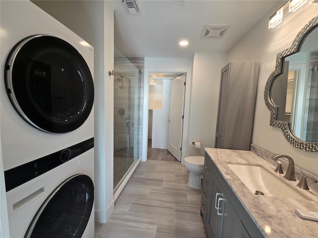 bathroom with stacked washer / drying machine, toilet, a shower with door, and vanity