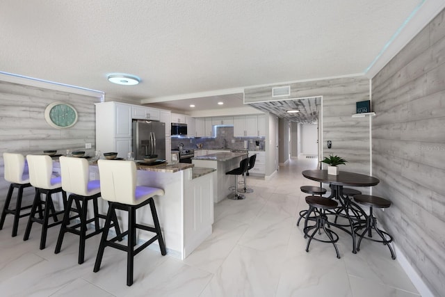 kitchen featuring a textured ceiling, white cabinets, appliances with stainless steel finishes, dark stone counters, and a breakfast bar area