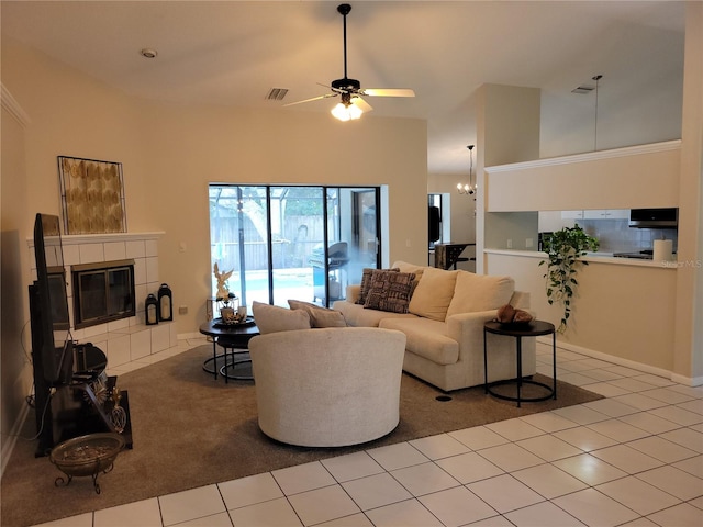 living room with a towering ceiling, light tile patterned floors, ceiling fan with notable chandelier, and a tiled fireplace