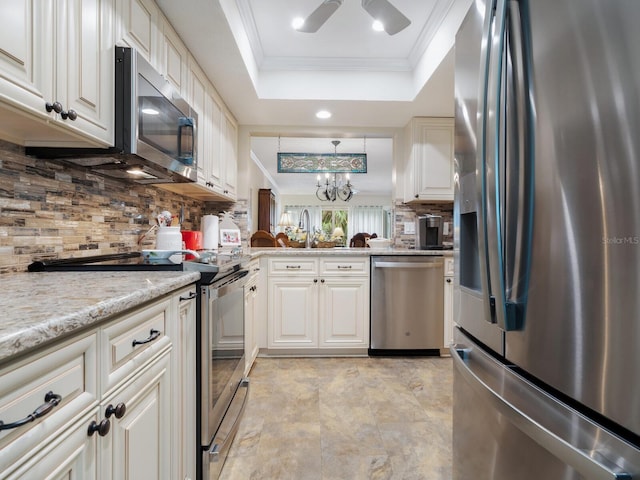 kitchen with tasteful backsplash, ornamental molding, a raised ceiling, stainless steel appliances, and light stone countertops