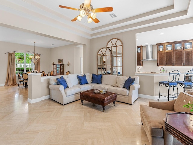 living room with a raised ceiling, light parquet flooring, and ceiling fan with notable chandelier