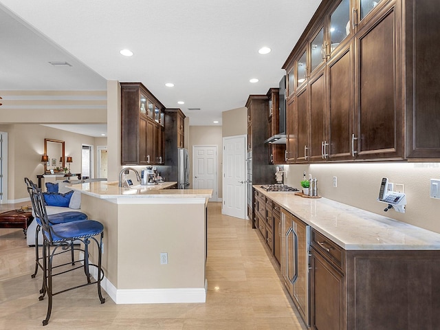 kitchen with light stone countertops, appliances with stainless steel finishes, dark brown cabinets, and wall chimney exhaust hood