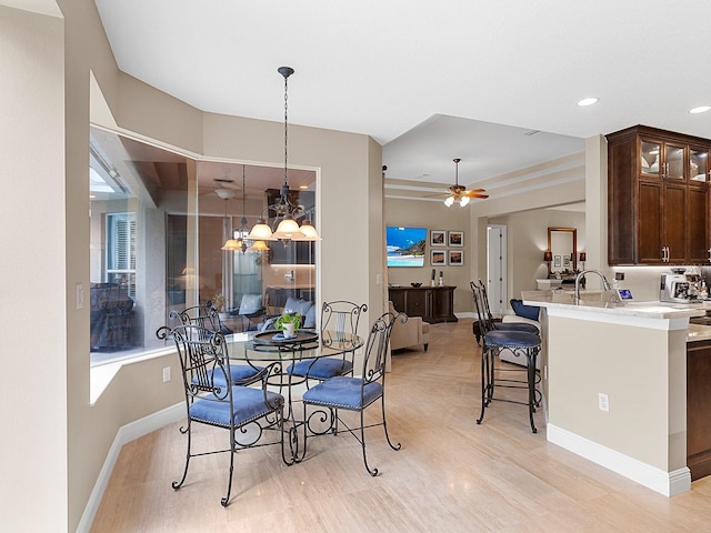 dining space with sink, ceiling fan with notable chandelier, and light wood-type flooring