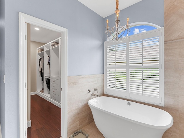 bathroom with a bath, plenty of natural light, tile walls, and an inviting chandelier