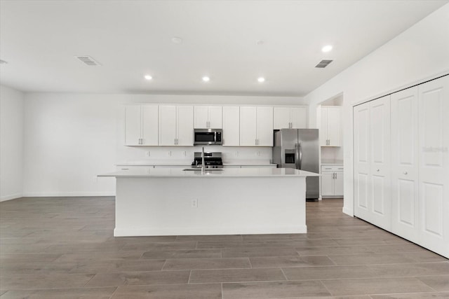 kitchen with white cabinets, appliances with stainless steel finishes, sink, and an island with sink