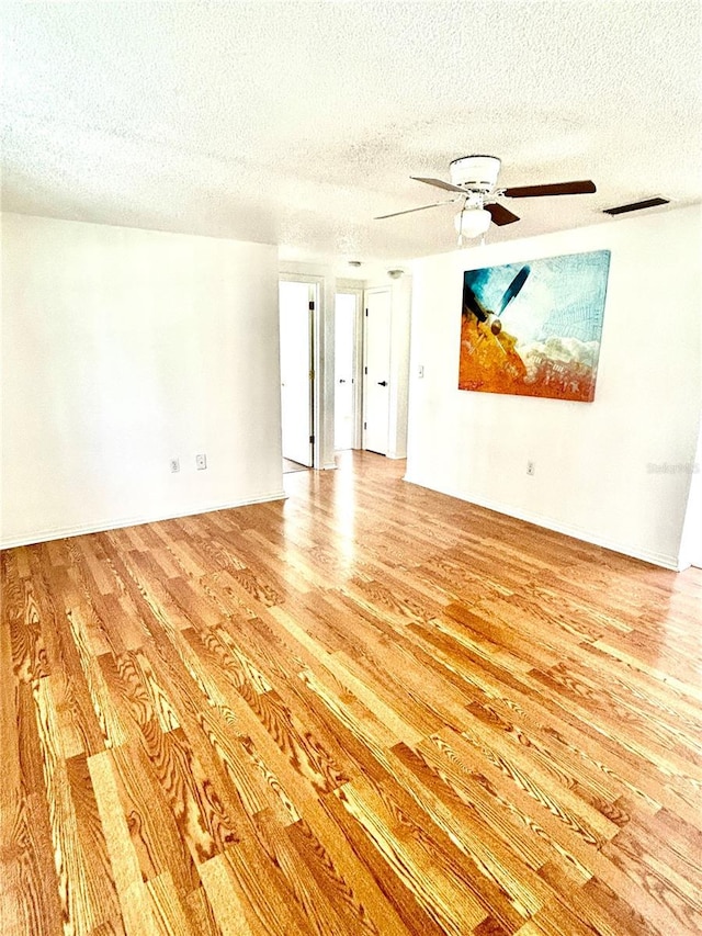 empty room with light wood-style floors, visible vents, a textured ceiling, and a ceiling fan