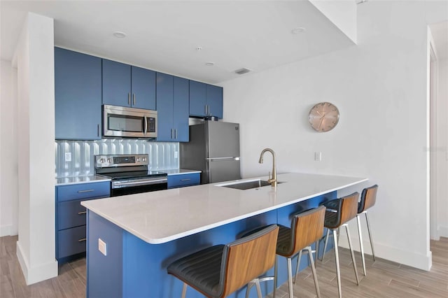 kitchen with blue cabinets, sink, a kitchen bar, appliances with stainless steel finishes, and kitchen peninsula