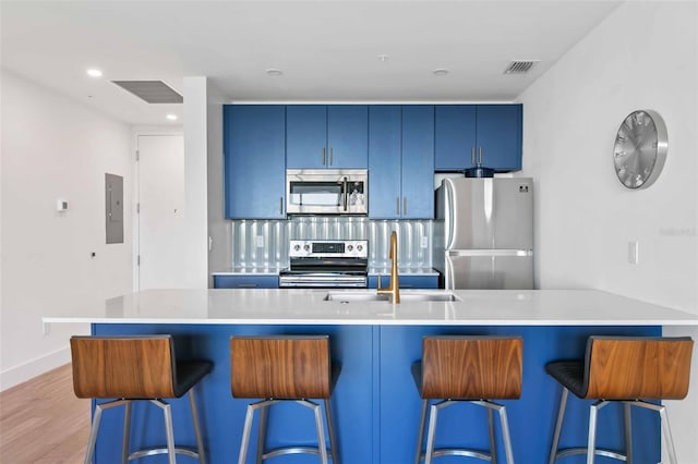 kitchen featuring a breakfast bar area, appliances with stainless steel finishes, blue cabinetry, decorative backsplash, and wood-type flooring