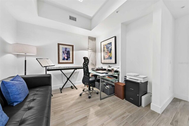 office area featuring light wood-type flooring and a tray ceiling