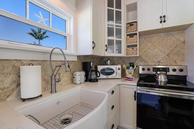 kitchen featuring electric range, sink, light stone countertops, backsplash, and white cabinets