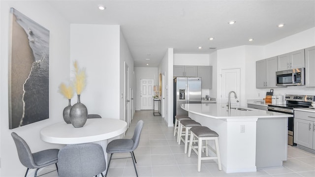 kitchen with a kitchen bar, stainless steel appliances, an island with sink, sink, and light tile patterned flooring