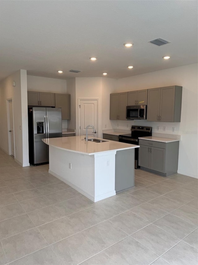 kitchen with light tile patterned floors, sink, appliances with stainless steel finishes, and an island with sink