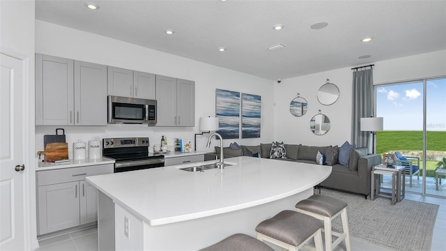 kitchen with a center island with sink, a breakfast bar, sink, appliances with stainless steel finishes, and light tile patterned floors